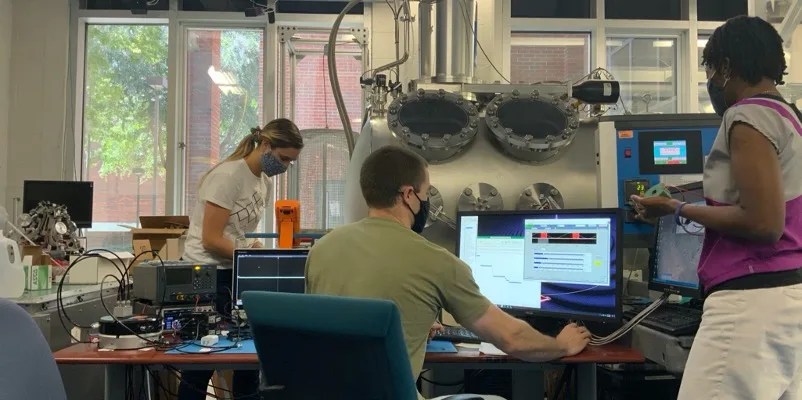 Photograph of two women and one man in a testing lab with computers and hardware on the desks
