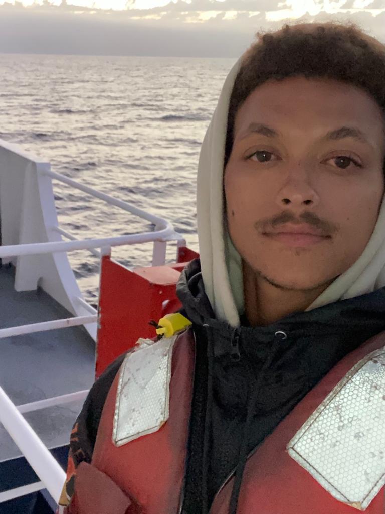 Photo of a man in a winter jacket on a boat on the icy ocean.
