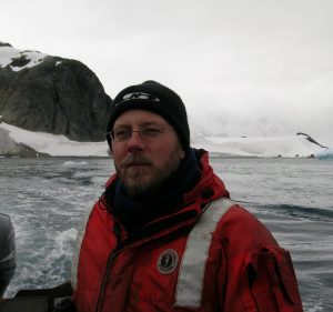 Photo of a man in an orange winter jacket and a stocking cap with an ocean in the background
