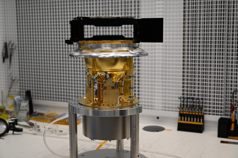 An instrument sits in the middle of the photo. It has a black top, gold middle section, and silver bottom and legs.